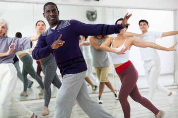 Portrait of cheerful adult african american man enjoying active dancing during group training in dance studio