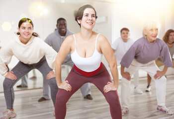 Obraz premium Cheerful sporty young Hispanic woman having fun and dancing hip hop during workout in group dance class for adults