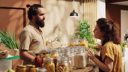 Client talking with seller in eco friendly shop, inquiring about food items ethical sourcing. Green living man in local store chatting with storekeeper about bulk products