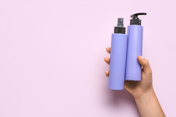 Female hand with bottles of cosmetic products on lilac background, closeup