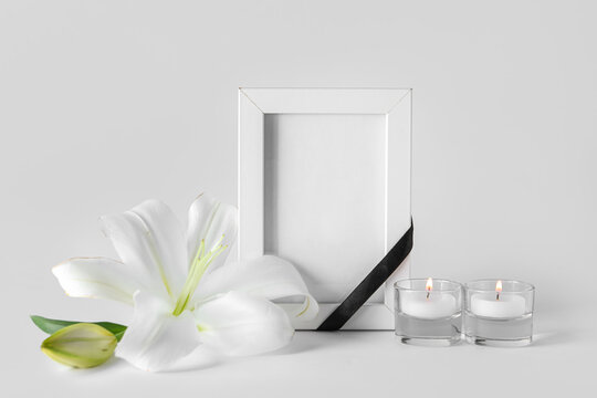 Blank funeral frame, burning candles and beautiful lily flowers on grey background
