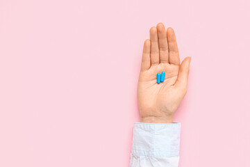 Female hand with blue pills on pink background