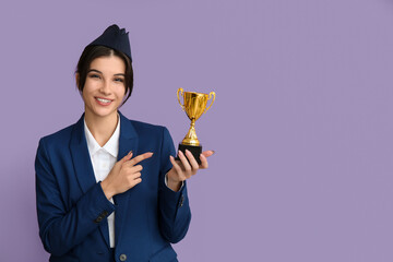 Young stewardess pointing at gold cup on lilac background