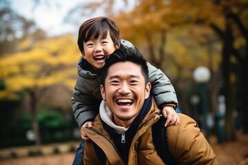 Happy Asian Father Carrying His Son on His Back in the Park