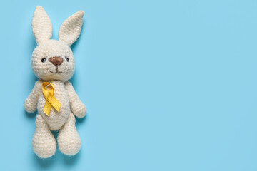 Obraz premium Toy bunny with golden ribbon on blue background. Childhood cancer awareness concept
