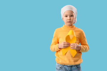 Cute little girl after chemotherapy with yellow ribbon on blue background. Childhood cancer awareness concept