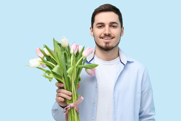 Young man with bouquet of beautiful tulips on blue background. International Women's Day