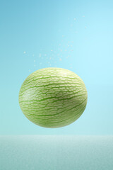 A whole green melon in a splash in water, set against a clear blue background, depicting a refreshing summer vibe.
