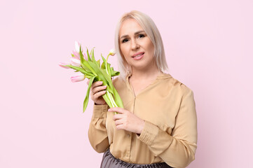 Mature woman with bouquet of beautiful tulips on pink background. International Women's Day