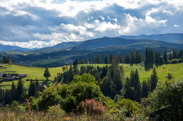 Rural landscape with cozy houses at the Mountain village on the green sunny hills with forest under blue sky with clouds. Carpathian Mountains, Ukraine 
