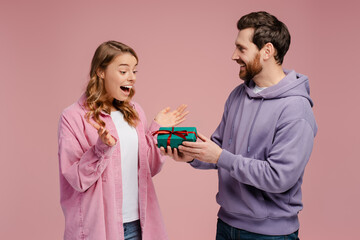 Smiling man giving gift box to overjoyed beautiful woman. Portrait of happy romantic couple...