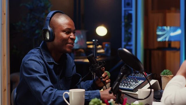 African american man recording podcast, adjusting microphone to ensure optimum sound quality for audience listening at home. Content creator using professional audio producing devices