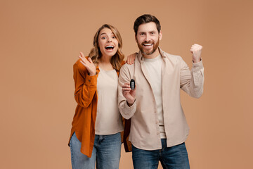 Portrait of overjoyed couple holding car key isolated on beige background	. Advertisement concept  - obrazy, fototapety, plakaty