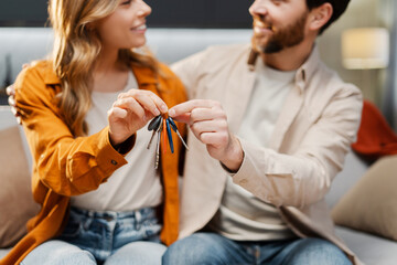 Happy young family holding keys from new home, selective focus. Attractive smiling man and woman...