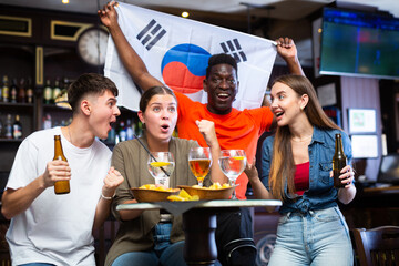 Group of excited football fans having fun in sports bar, celebrating victory of favorite South...