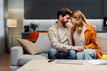 Naklejka na ściany i meble Young happy couple hugging, holding hands sitting face to face on comfortable sofa at cozy home. Love, dating, Valentine's day concept