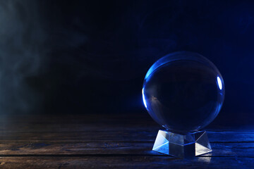 Magic crystal ball on wooden table against dark background, space for text. Making predictions