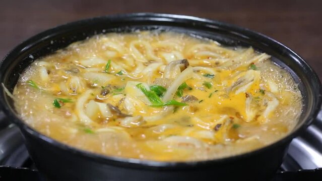 검은색 냄비에서 버섯 칼국수가 끓고 국자로 뒤적이는 