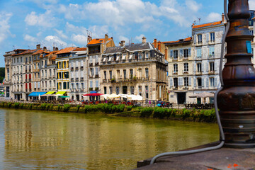 View from bridge over Nive river of peculiar architecture of houses on Bayonne quay on summer day,...