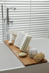 Wooden tray with spa products and book on bath tub in bathroom