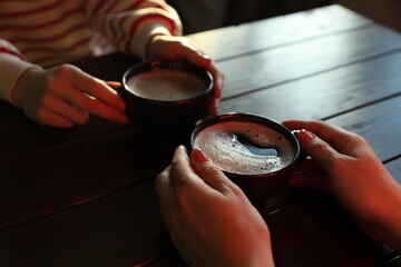 Women with cups of hot coffee at wooden table, closeup