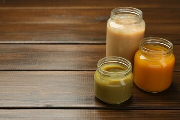 Tasty baby food in jars on wooden table. Space for text