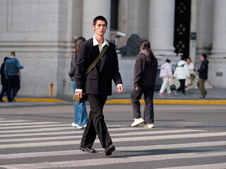 Portrait of handsome Chinese young man with black short hair wearing black blazer walking on street...