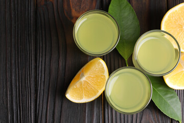 Tasty limoncello liqueur, lemon and green leaves on dark wooden table, flat lay. Space for text