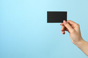 Woman with blank black business card on light blue background, closeup. Mockup for design