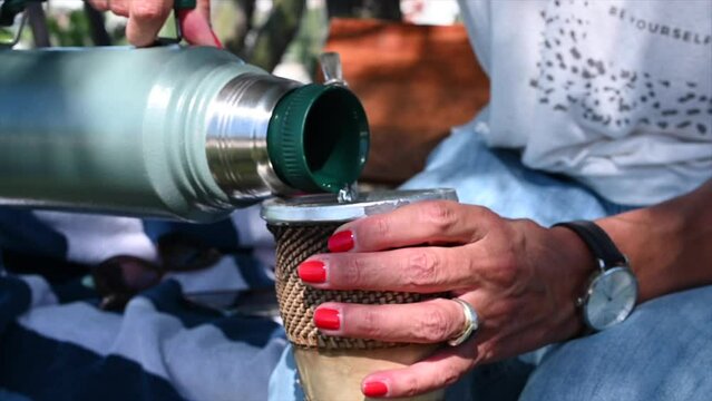 horizontal video in slow motion of woman's hands with painted nails drinking Argentine mate in the shade of a tree in summer 2