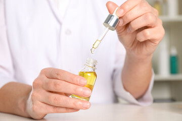 Fototapeta premium Dermatologist developing cosmetic oil at white table indoors, closeup