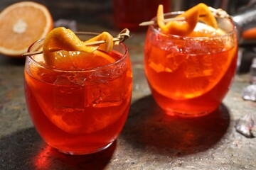 Aperol spritz cocktail, ice cubes and orange slices in glasses on grey textured table, closeup