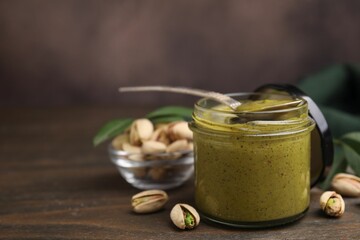 Tasty pistachio cream in jar, spoon and nuts on wooden table, closeup. Space for text