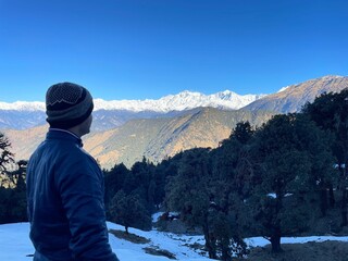 man looking into the distance at snowy mountains in nepal, surrounded by green trees