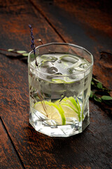 Pure still water with lemon and ice in a glass on a wooden background. Dark rustic style