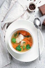 Chicken broth with vegetables and herbs in a white bowl. Transparent soup with homemade chicken, top view