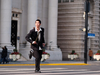 Portrait of handsome Chinese young man with black short hair wearing black blazer running across...