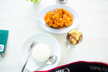 Top view of fried shrimp with sweet and sour seasoning served on a white plate with a plate of rice and a glass of avocado juice