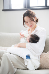 Vertical view of a woman sitting on a sofa feeding a baby.