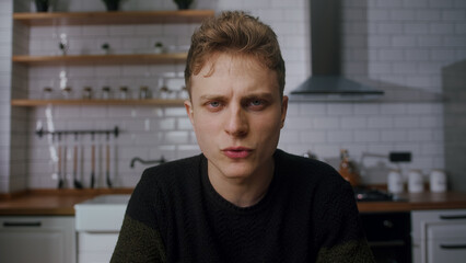 Young blonde man sit in a modern office kitchen looking to camera talking. Confident male have video conference, remote chat, webcam view	
