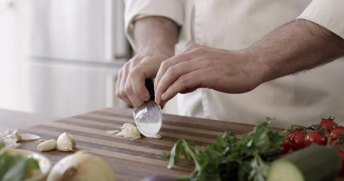 Chef, hands and chopping vegetables for preparation on kitchen counter for nutrition, health or salad. Person, fingers and knife or cut garlic on board for culinary cuisine, professional or skills