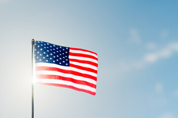 Fototapeta premium Pride and Patriotism. American flag unfurled against the sunlight and blue sky.