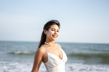 Fototapeta na wymiar Portrait of young beautiful woman in white dress standing on the beach. 