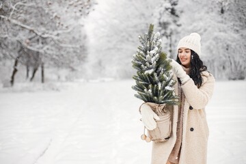 Portrait of a woman walking in forest at winter day and holding a Christmas tree in a pot