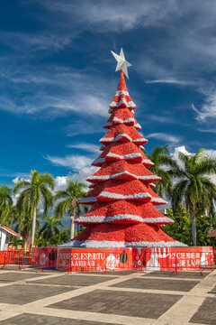 Large red Christmas tree set up by Coca Cola company in city center square, shot on sunny day, blue sky in the background.