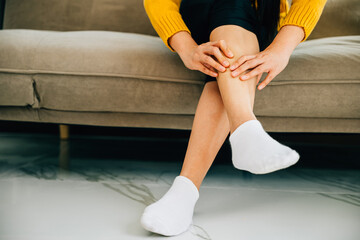 Close-up of woman on sofa holds her ankle injury feeling pain. Depicting health care varicose vein...