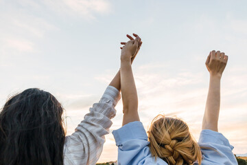 Two young women enjoying nature with the hands up, in a field at sunset. close-up
