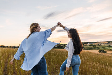 two young women dancing and having fun in a field at sunset