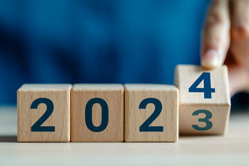 Close up view of hand flipping cube wooden 2023 to 2024 with dartboard icon, the end of 2023 and...