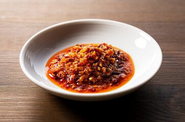 An edible chili oil in a ceramic dish placed on a wooden background.